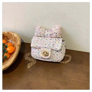 Detail of pink tweed crossbody bag with bow accent and gold chain strap in home setting