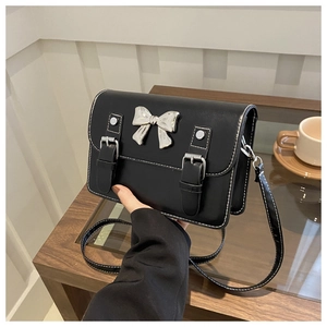 Close-up of black PU leather crossbody bag with white stitching and silver bow detail