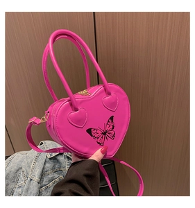Detail of bright pink heart-shaped handbag featuring black butterfly print and gold zipper