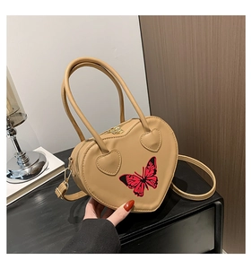Detail of beige heart-shaped handbag featuring butterfly print and top handle