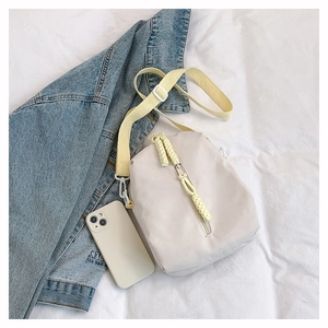Detail of minimalist cream nylon crossbody bag with vibrant yellow adjustable strap and cords