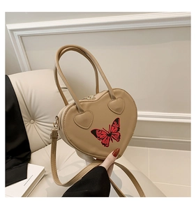 Detail of heart-shaped handbag in khaki faux leather featuring a butterfly patch and strap