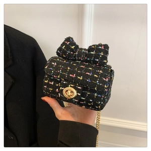 Mini black tweed crossbody bag with large bow detail and gold chain held by model