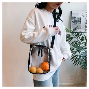 Detailed view of a clear PVC crossbody bag with black trim worn by a model in casual style