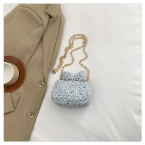 Detail of blue tweed mini crossbody bag with a bow-shaped flap and gold chain strap