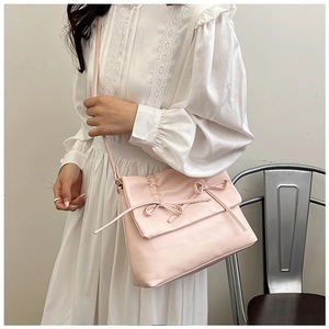 Dettaglio della borsa in ecopelle rosa con fiocchi e patta a pieghe su un abito bianco