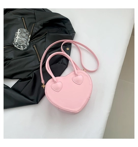 Pink heart-shaped handbag with top handle and crossbody strap over a black leather jacket