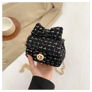 Detail of tweed mini bag with bow accent and gold chain strap held in a cafe setting
