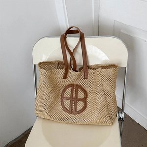 Woven straw tote bag with brown leather handles and circular logo on a minimalist chair