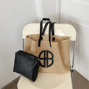 Straw woven tote bag with black leather handles and matching zipper pouch on a chair