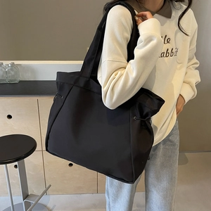 Large black minimalist nylon tote bag shown on model in a modern interior setting