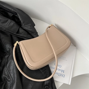Minimalist beige shoulder bag with gold hardware placed on a black leather jacket
