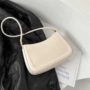 Minimalist beige leather shoulder bag with gold hardware on black jacket background