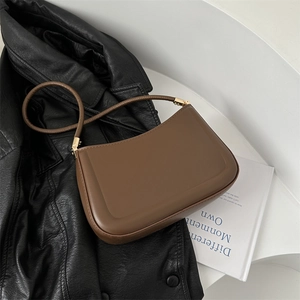Minimalist brown leather shoulder bag with gold hardware on a sleek white pedestal