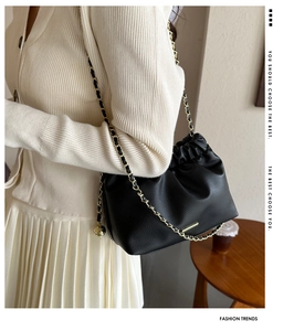 Détail du sac seau en cuir grainé noir avec cordon de serrage et chaîne dorée élégante