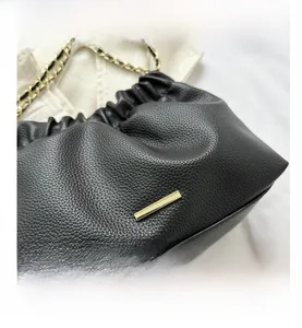 Détail d'un sac à main en cuir noir grainé avec barre dorée et bandoulière chaîne