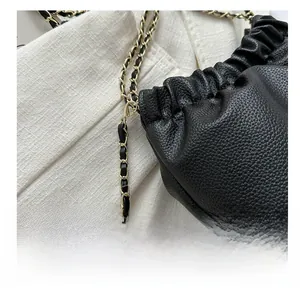 Gros plan sur sac seau en cuir grainé noir avec chaîne dorée et détail de boule