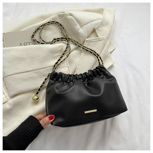 Détail du sac bandoulière en cuir grainé noir avec chaîne dorée et boule en métal ajustable