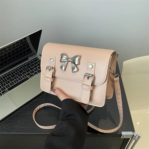 Chic beige crossbody satchel with silver bow and dual buckle straps in office setting