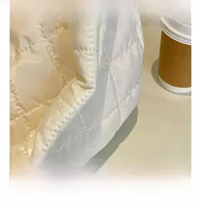 Close-up of white quilted fabric with square padding and soft glossy texture on bag