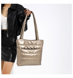 Detailed side view of champagne gold quilted tote bag on model in black leather jacket