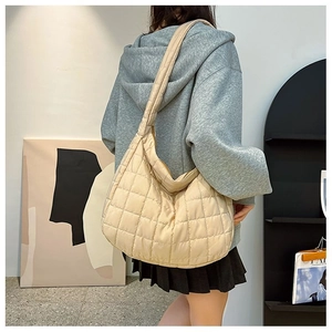 Close-up of beige quilted puffer hobo bag with classic square stitching worn by model