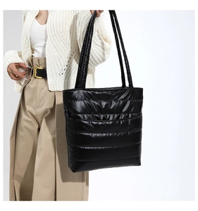 Detailed view of black quilted puffer tote bag with glossy finish and thick shoulder strap