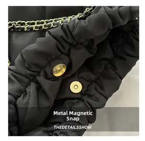 Detail van de gouden magneetsluiting op de zwarte gewatteerde bucketbag met ketting