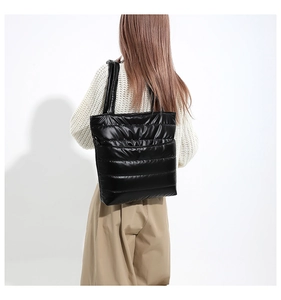 Black quilted down tote bag in shiny nylon with shoulder straps worn by a model