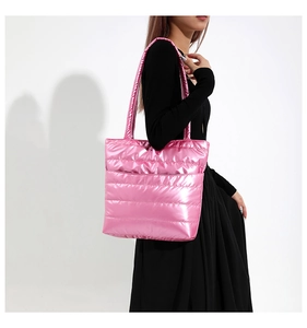 Detail of bright pink quilted tote bag in shiny nylon worn by a model in black dress