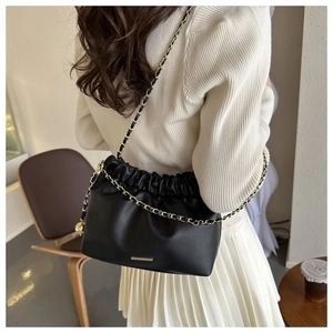 Détail du sac seau noir en cuir grainé avec bandoulière chaîne dorée et cordon de serrage