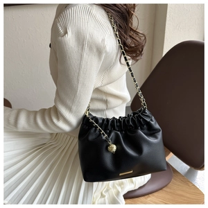 Détail du sac seau en cuir grainé noir avec chaîne dorée et design plissé élégant