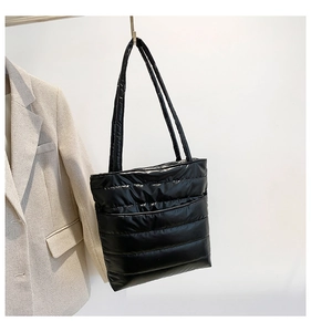 Detail of black quilted puffer tote bag with glossy nylon texture and padded shoulder strap