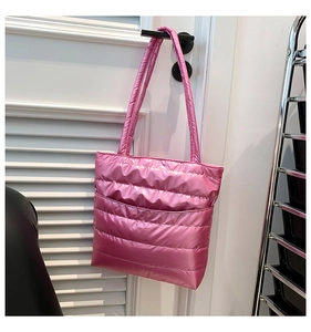 Pink quilted down tote bag made of lightweight nylon hanging on a wooden door handle