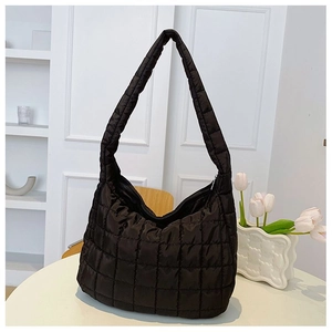 Detail of black quilted puffer tote bag with wide shoulder strap on a white table