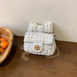 Chic tweed mini crossbody bag with a large bow and golden chain strap on a table