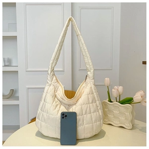 Quilted beige puffer tote bag size comparison with smartphone on soft textured background