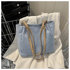 Detail of light blue twill canvas tote bag with brown leather straps in a metal cart