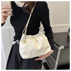 Détail du sac seau en cuir crème avec chaîne dorée et pendentif boule élégant