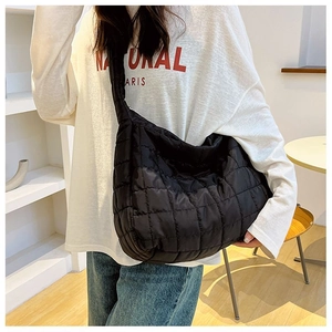 Detail view of a black quilted puffer crossbody bag with a wide shoulder strap worn by a model