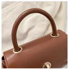 Close-up of brown leather handbag handle with gold eyelets and round metallic twist lock