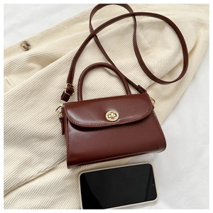 Detail of dark brown mini crossbody bag with golden round lock and phone for scale