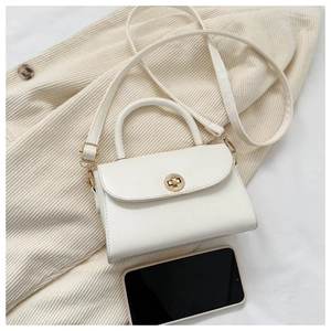 Macro detail of cream mini crossbody bag with golden ring lock and phone for size
