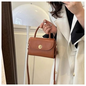 Detail view of caramel leather handbag with gold circular metal buckle and top handle
