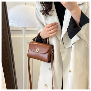 Detail view of a vintage brown leather crossbody bag with a golden circular metal buckle