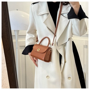 Detail of caramel leather mini square bag with golden twist lock on a white trench coat
