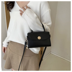 Detail of a black leather crossbody bag with a gold round clasp shown on a model