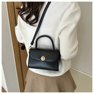 Detail of black leather crossbody bag featuring a circular gold metal twist lock and handle