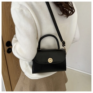 Retro black leather crossbody bag featuring a round metal twist lock on a white sweater