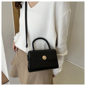 Detail of a minimalist black leather crossbody bag with a round gold metal twist lock